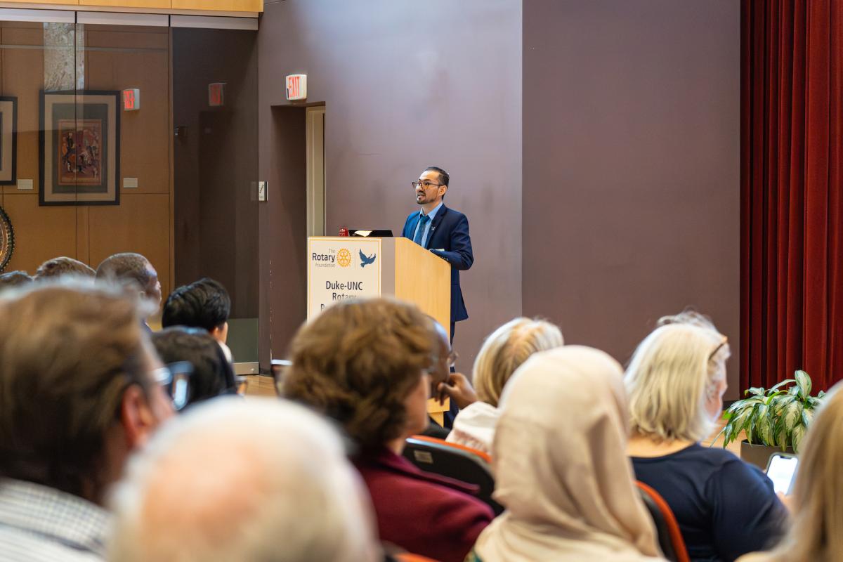 Man speaking to a seated audience while standing behind a lectern