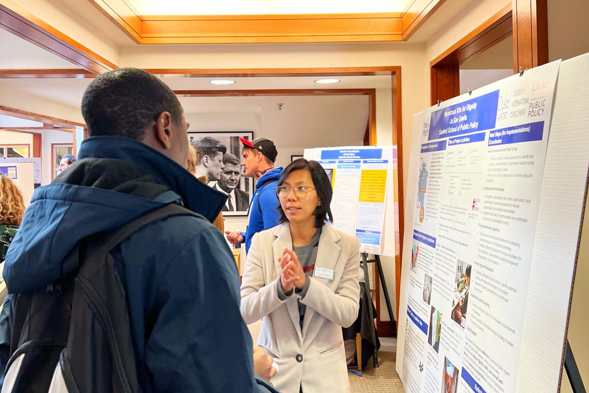 Person standing and talking to another person next to a poster.