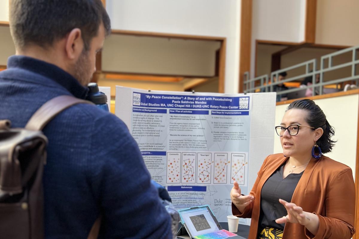 Person standing in front of a poster talking to another person