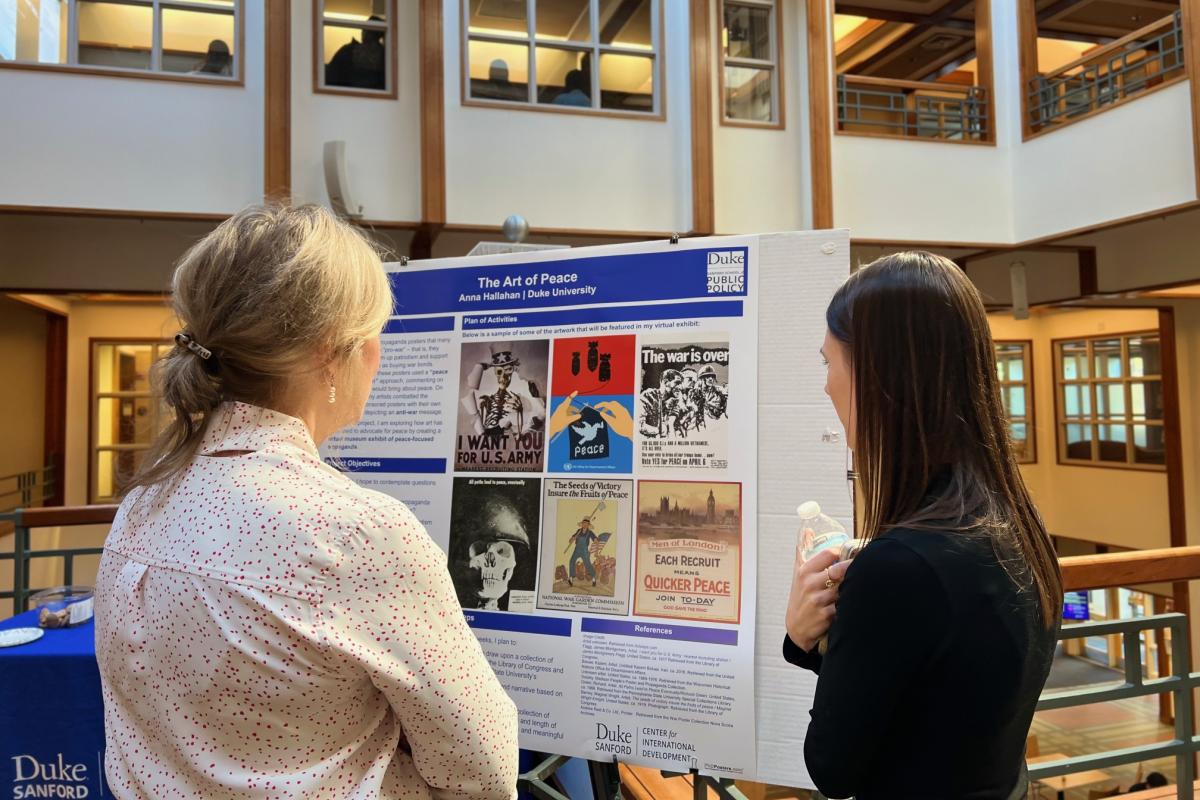 Two people standing and looking at a poster. 