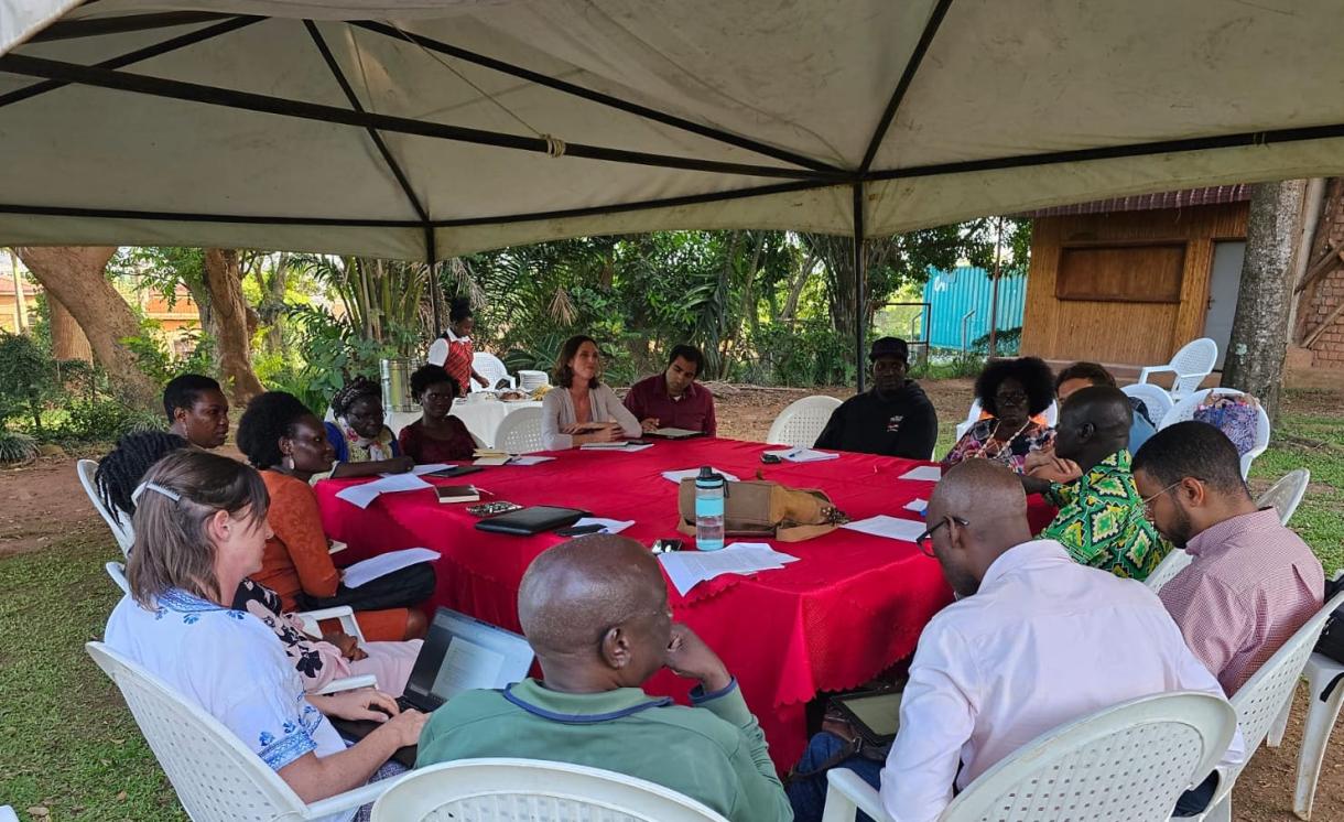 Workshop participants sitting and talking around a table under a tent outside. 